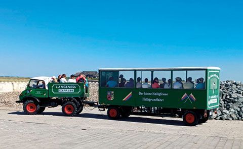 Ein grüner Lastwagen, der einen grünen Anhänger mit Menschen darauf zieht.