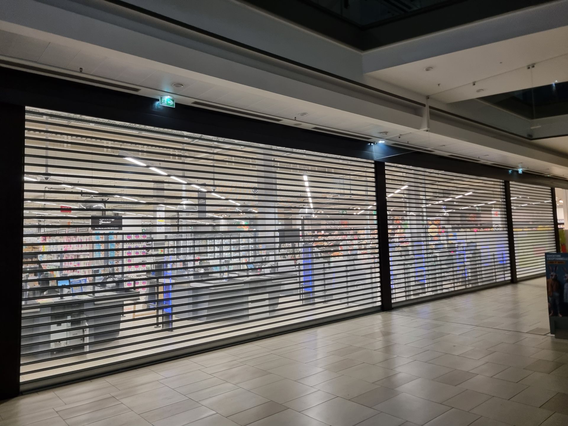 Façade de magasin fermée avec grilles de sécurité dans un centre commercial.