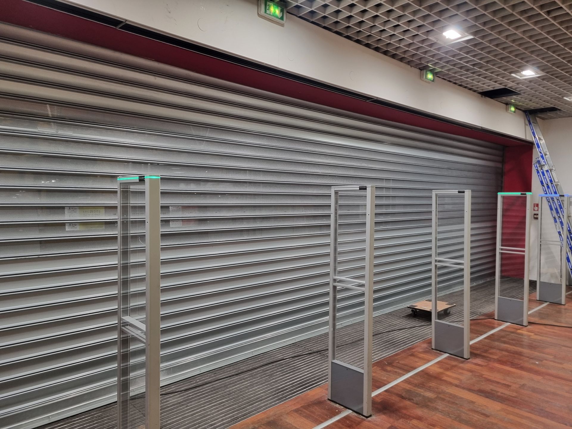 Magasin fermé avec portails et capteurs de sécurité. Porte métallique coulissante, liseré rouge au-dessus.