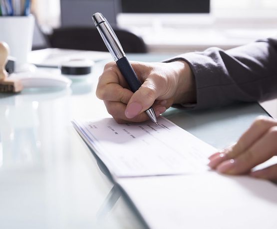 Una persona está escribiendo un cheque con un bolígrafo en un escritorio.