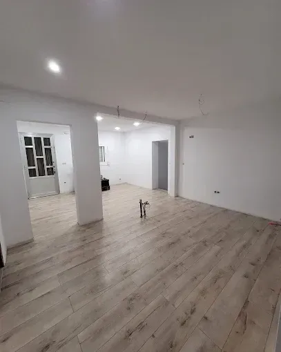 Una habitación vacía y luminosa, con paredes blancas, suelo de madera clara y una distribución diáfana con puertas.