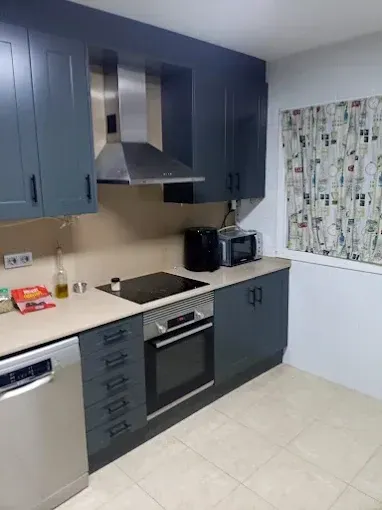 Una cocina moderna con armarios azul oscuro, electrodomésticos de acero inoxidable, vitrocerámica y cortinas estampadas.