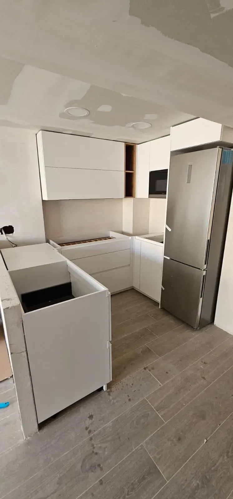 Una cocina sin terminar con armarios blancos y un suelo de baldosas con aspecto de madera.