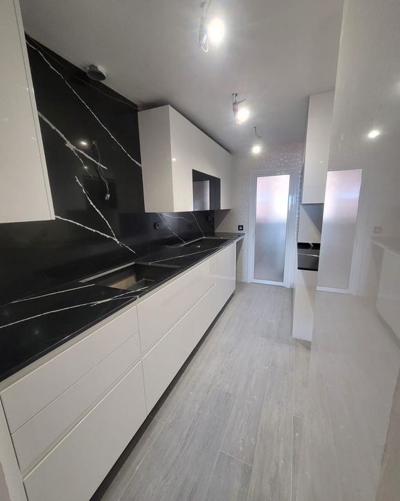 Una cocina sin terminar con armarios blancos y un suelo de baldosas con aspecto de madera.