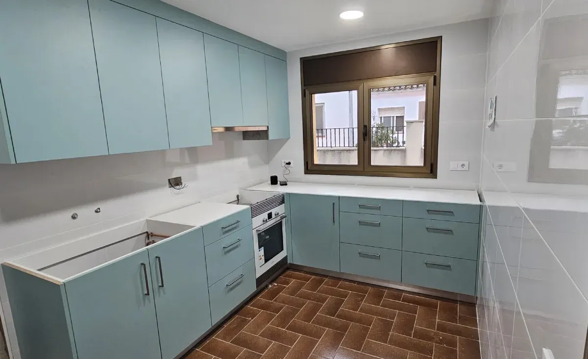 Una cocina con armarios azul claro, encimeras blancas, una estufa y suelo de baldosas marrones con estampado.