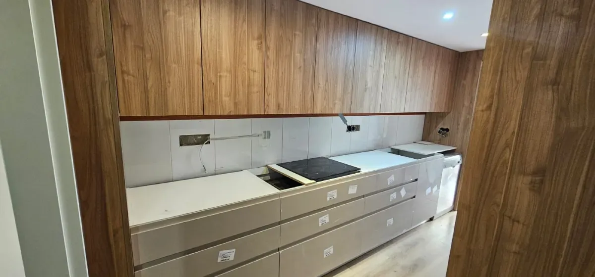 Una cocina moderna con armarios de madera, encimeras de color claro, salpicadero de azulejos y electrodomésticos integrados.