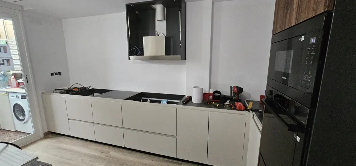 Una cocina moderna con armarios bajos de color blanco roto, una campana extractora negra y un horno alto negro.