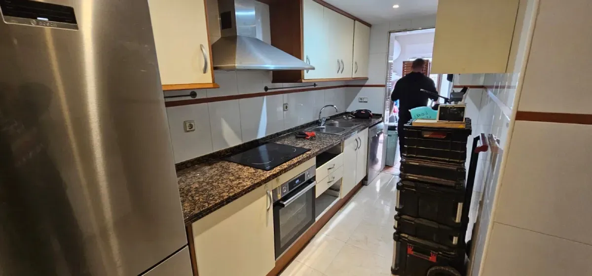 Una estrecha cocina tipo galera con armarios claros, encimeras de granito, electrodomésticos de acero inoxidable.