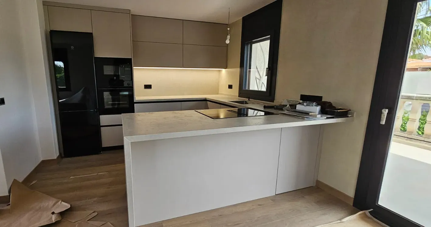 Cocina moderna con armarios de madera clara, encimeras blancas, una isla central y 