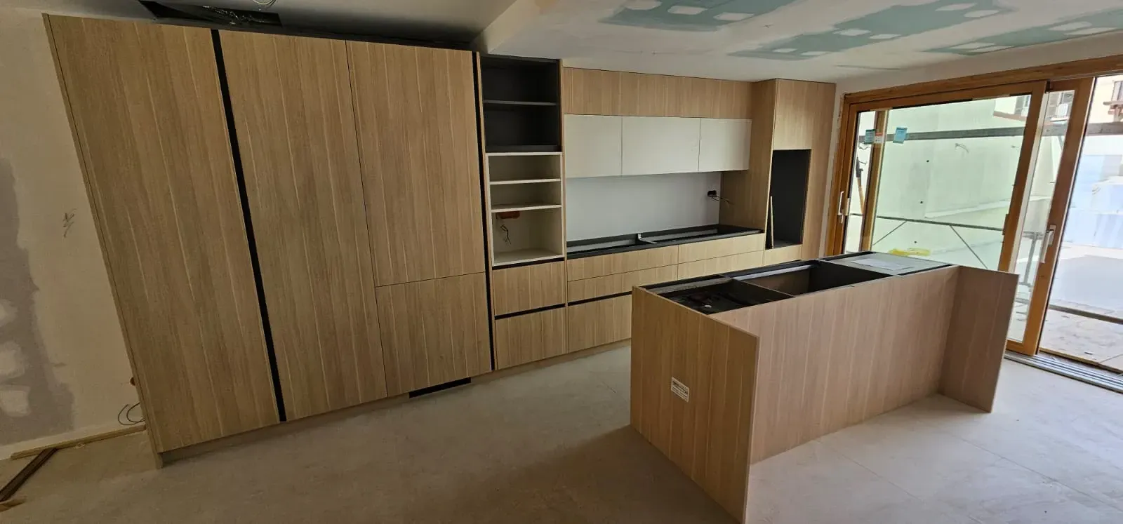 La cocina en construcción cuenta con gabinetes de madera clara, gabinetes superiores blancos, una estantería y una isla.