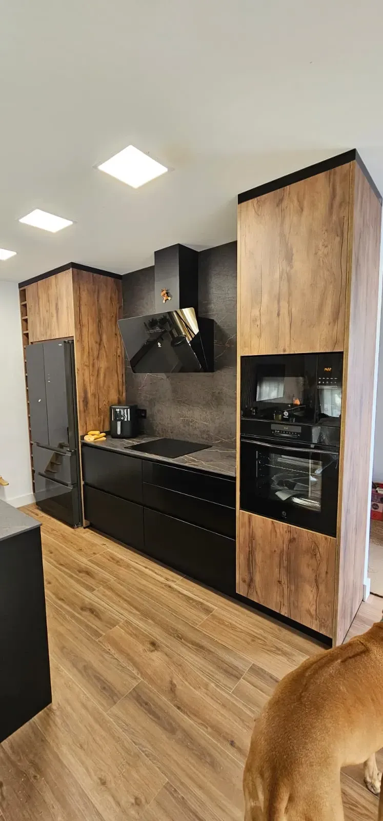 Una cocina moderna con armarios negros, horno empotrado, campana extractora elegante y detalles en madera de tonos claros.