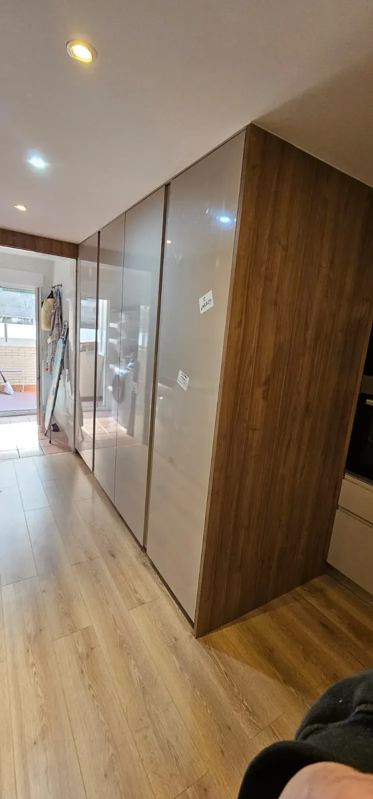 Una cocina con armarios altos de color gris claro, paneles laterales con vetas de madera y suelo de madera a juego.