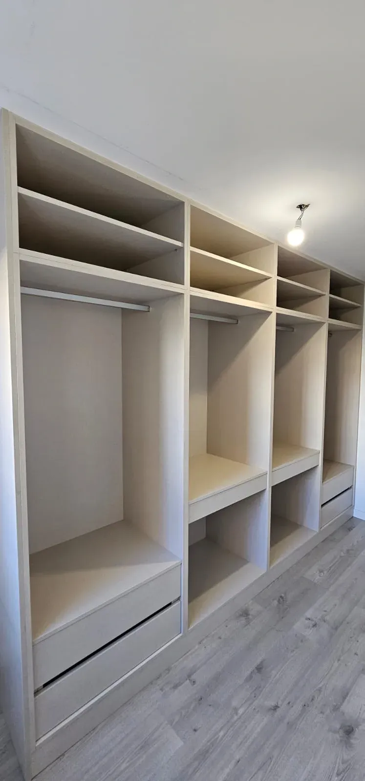 Un armario empotrado grande, moderno y de madera clara, con múltiples estantes, barras para colgar ropa y cajones inferiores.