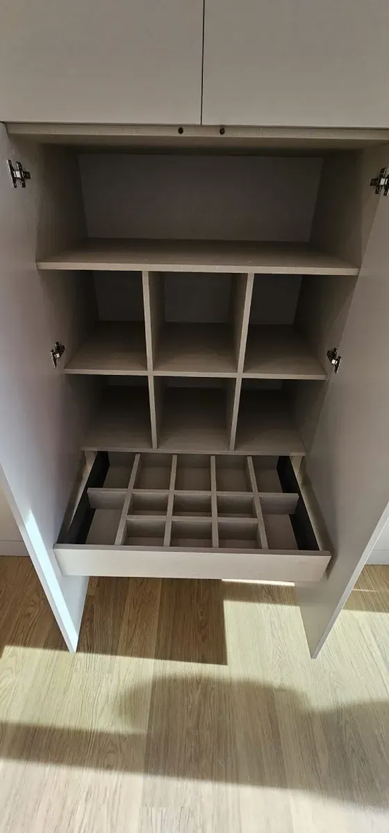 Un armario abierto de madera con varios estantes y un cajón extraíble con un inserto de almacenamiento tipo rejilla.