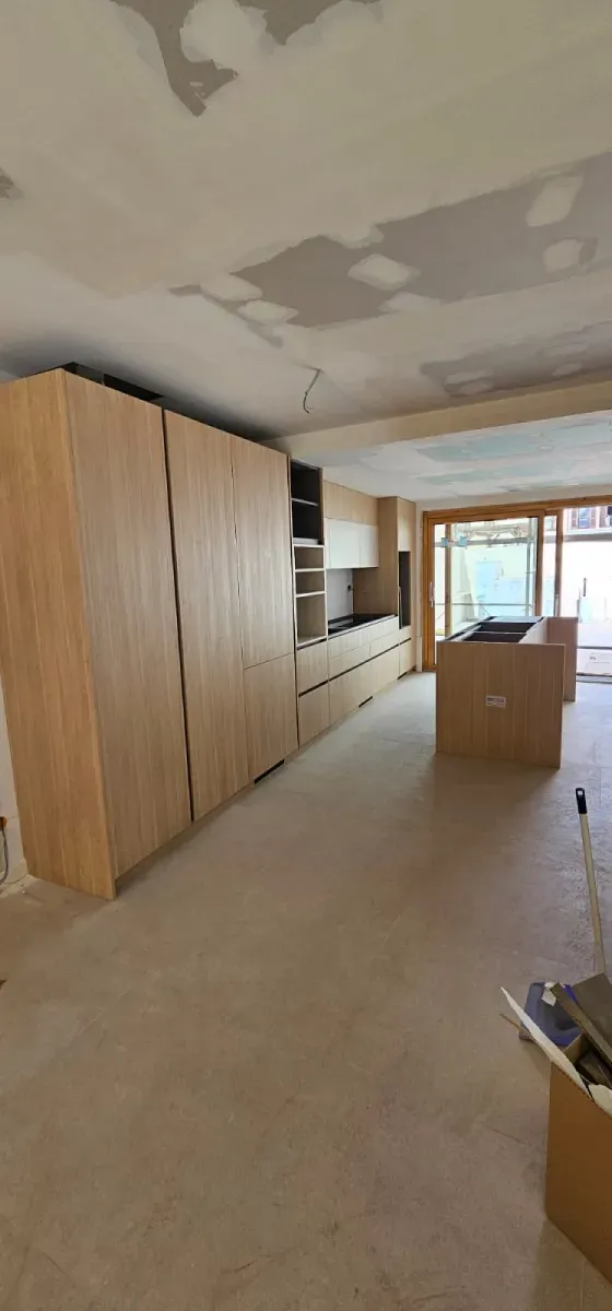 Una cocina moderna en proceso de renovación con armarios de madera clara, una isla central y un techo sin terminar.