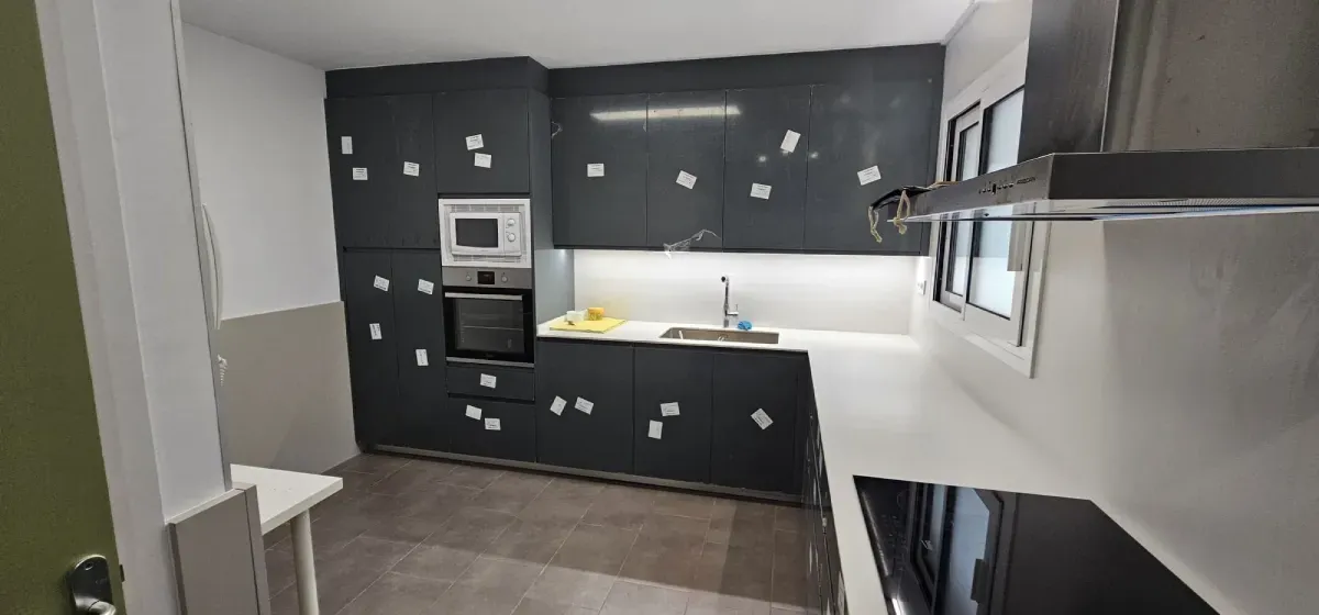 Una cocina moderna con armarios de color gris oscuro, horno y microondas empotrados, fregadero y encimera de color claro.