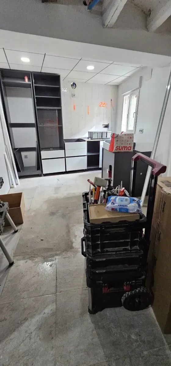 Una habitación en proceso de renovación con muebles de madera oscura y armarios blancos instalados contra la pared del fondo.