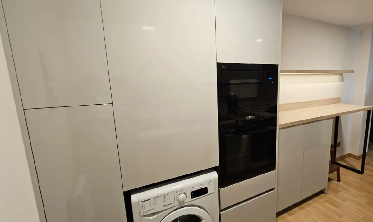 Una cocina moderna con armarios de color gris claro, horno empotrado, lavadora y encimera con estante.
