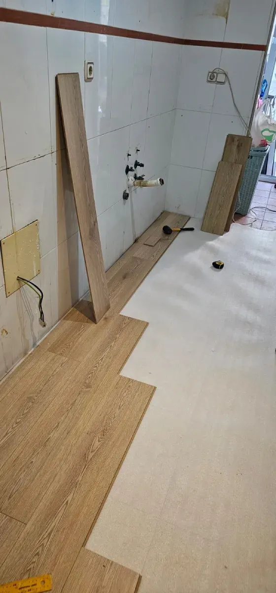 Reforma de cocina en la que se están instalando lamas de vinilo con aspecto de madera clara sobre una base blanca.