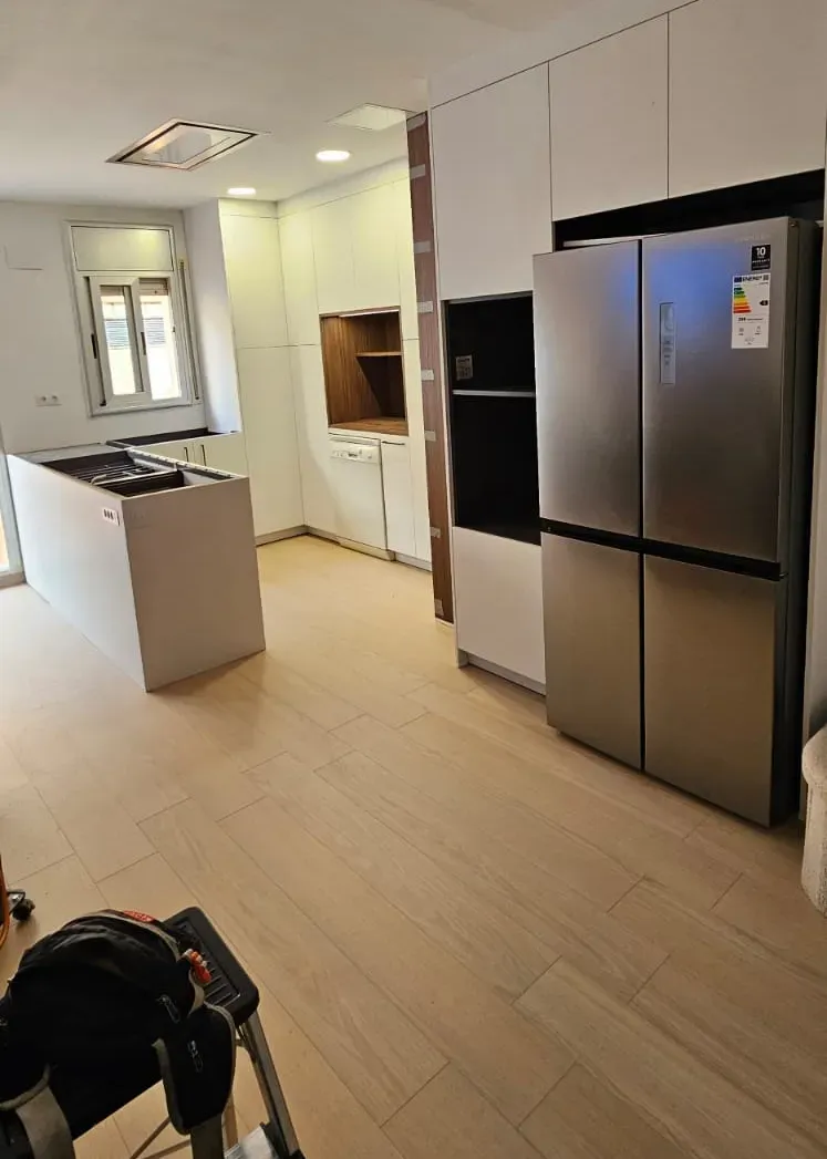 Una cocina cuenta con un refrigerador de acero inoxidable, gabinetes blancos, una isla central.