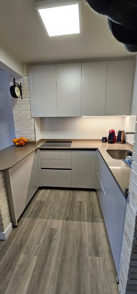 Una cocina en forma de U con armarios, encimeras grises y suelo laminado con aspecto de madera bajo una lámpara cuadrada.