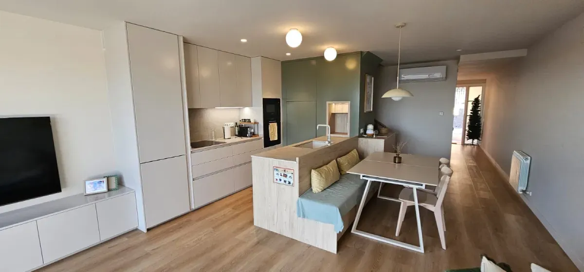 Cocina y comedor modernos de planta abierta con suelos de madera clara, detalles en verde y un rincón con banco empotrado.