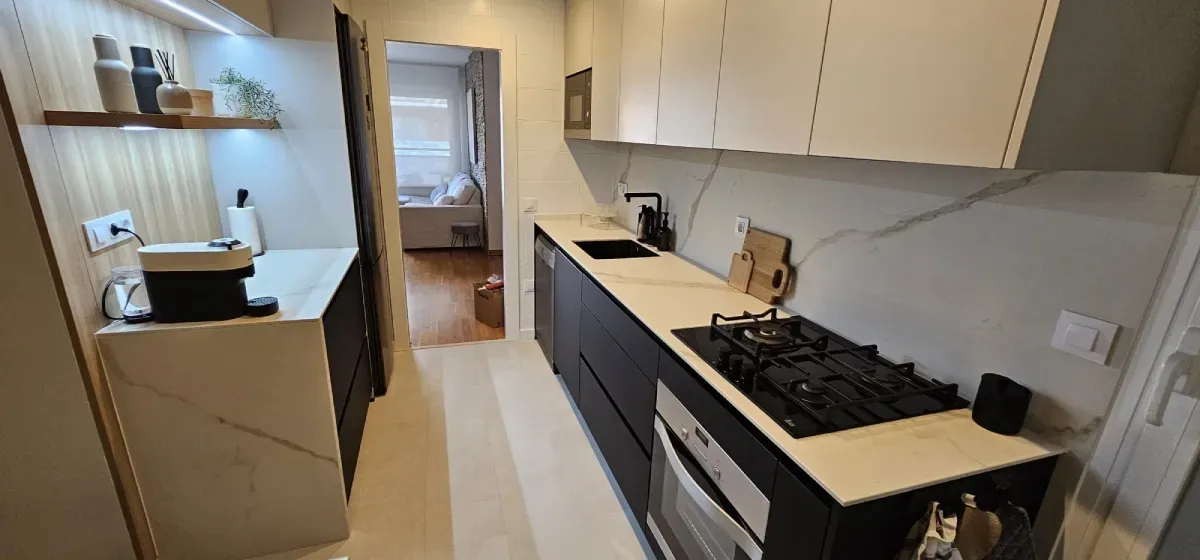 Una cocina tipo galera cuenta con gabinetes negros, encimeras blancas, cocina de gas y una puerta.