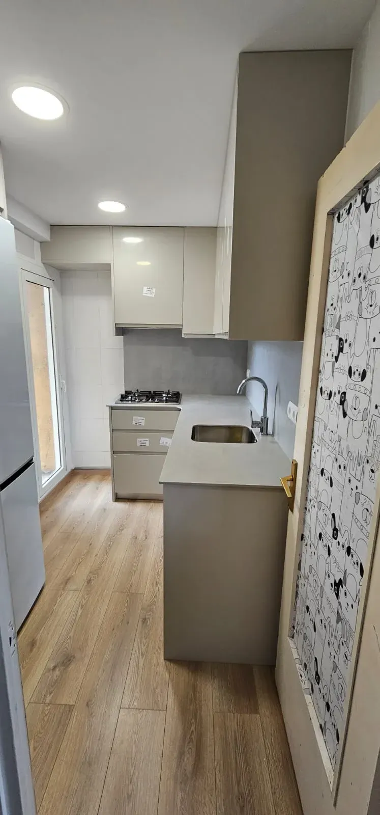 Una cocina estrecha con armarios, suelo con aspecto de madera, placa de gas y fregadero de acero inoxidable.