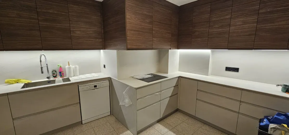 Una cocina en forma de L con armarios superiores con acabado de madera, armarios inferiores y encimeras blancas.