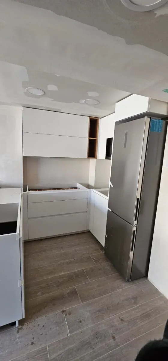 Una cocina en forma de L en construcción con gabinetes blancos, piso de baldosas y un refrigerador de acero inoxidable.