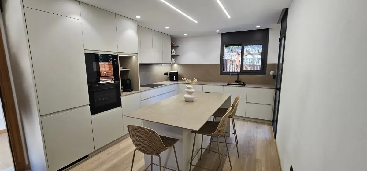 Cocina moderna y minimalista con isla central, armarios de color beige claro, electrodomésticos y suelo de madera clara.