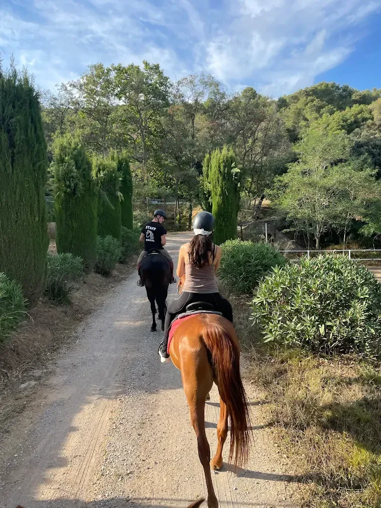 Dos personas montan a caballo por un camino de tierra.