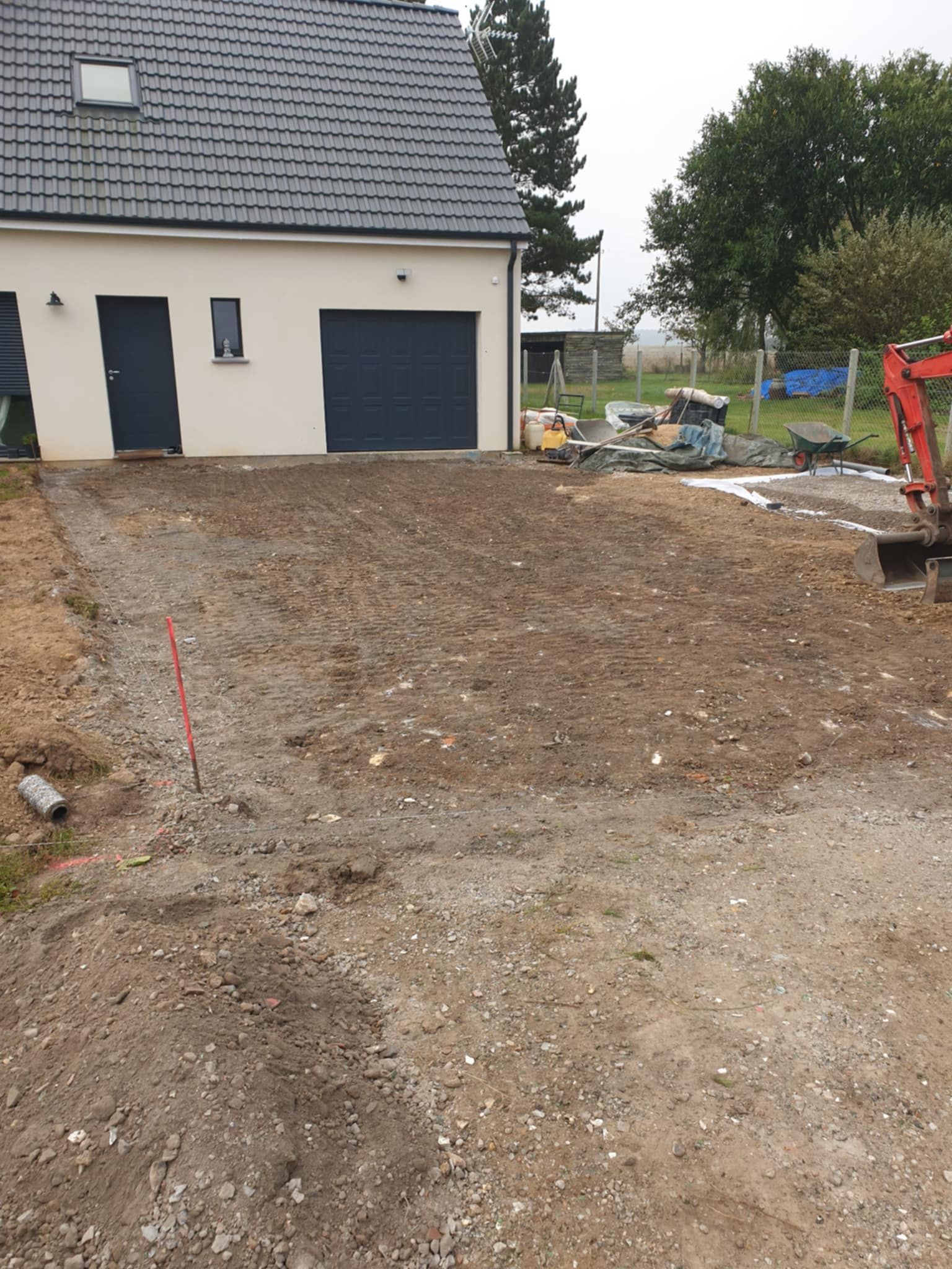 Allée en construction devant une maison avec garage et porte bleu foncé.