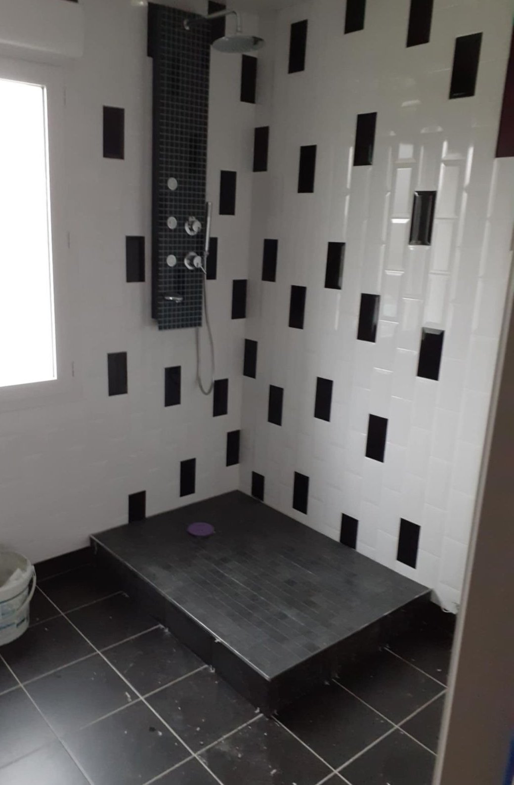 Douche avec sol carrelé noir, plateforme et murs d'accentuation ornés de rectangles noirs. Colonne de douche noire.