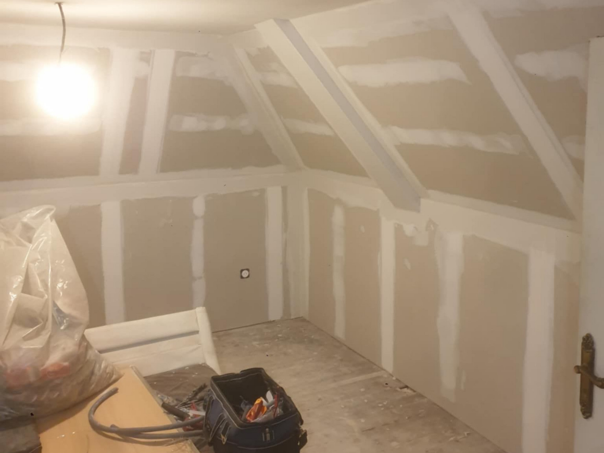 Pièce intérieure en construction, avec des plaques de plâtre sur les murs, une fenêtre et du parquet.