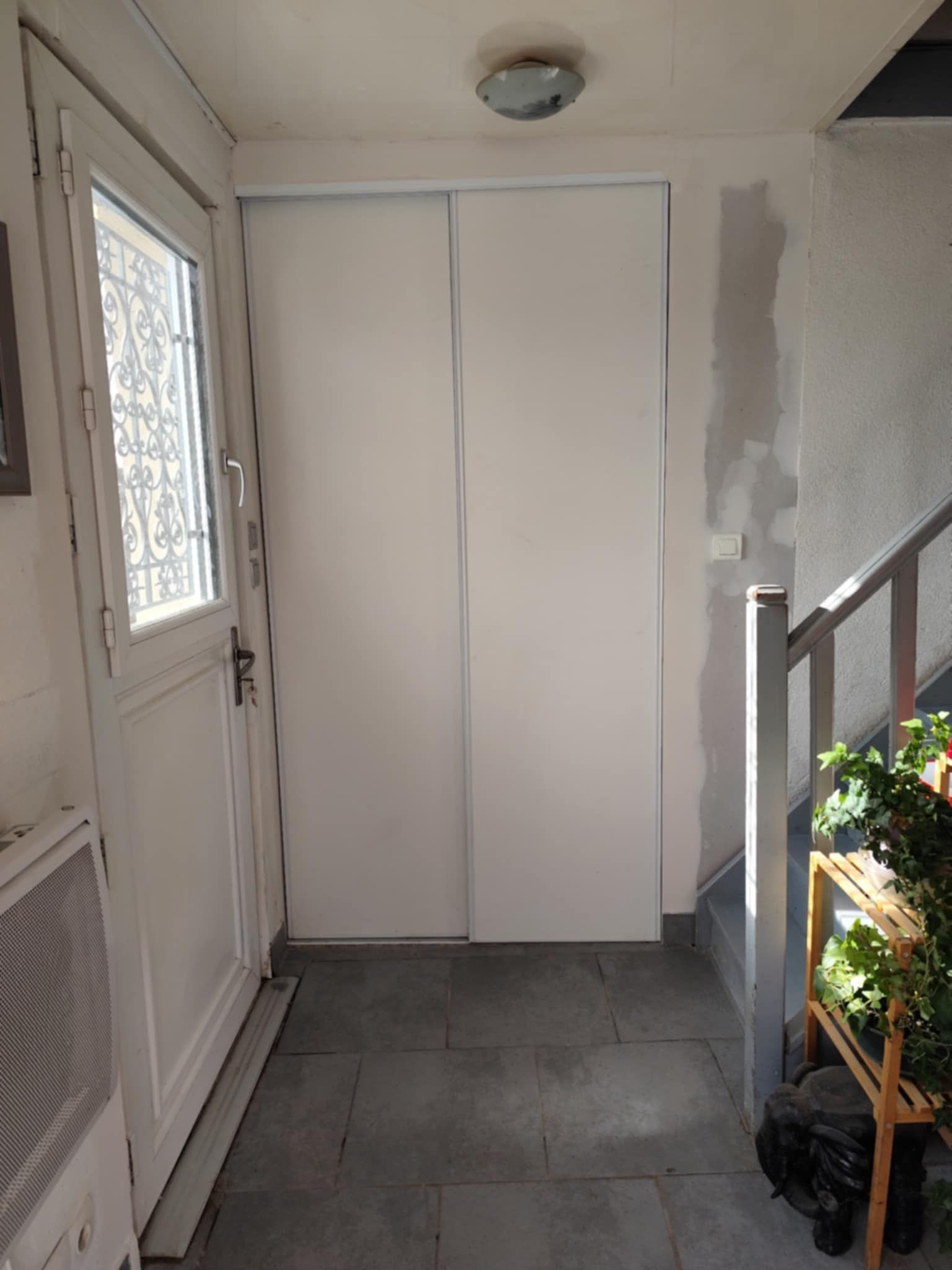 Couloir avec porte blanche, portes de placard, escalier et plantes.