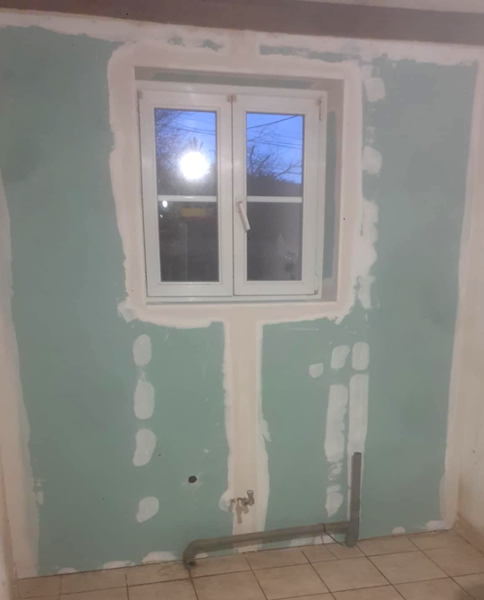 Intérieur en construction : cloison sèche avec joints collés, mur non fini, matériaux de construction au sol.