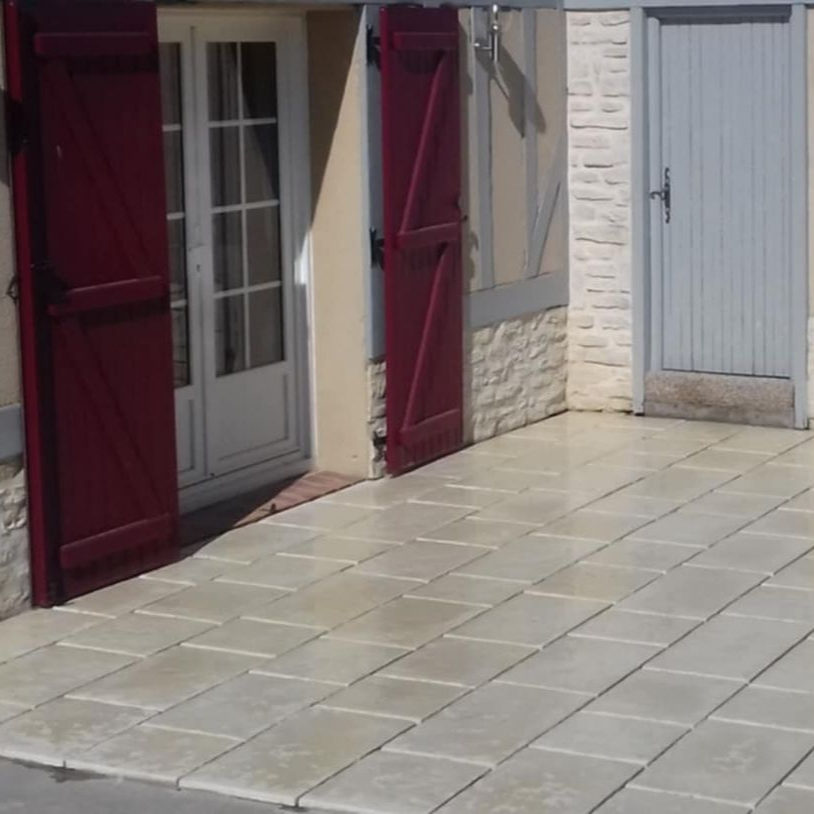 Entrée avec volets rouges et patio pavé gris. On distingue également une porte blanche et une porte grise.