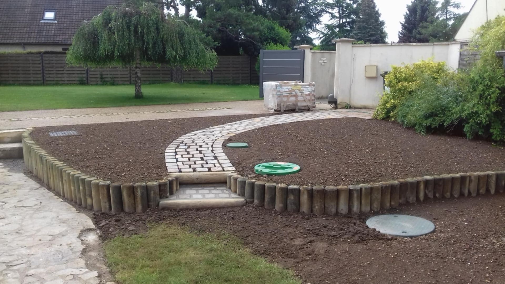 Parterre de jardin avec bordure en bois, chemin en pierre et saule pleureur.