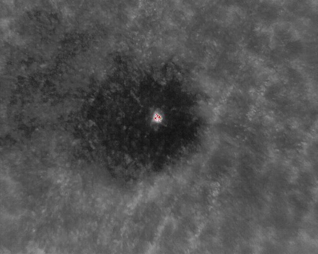 Dunkler Krater auf einer Planetenoberfläche mit einem hellen Punkt in der Mitte.