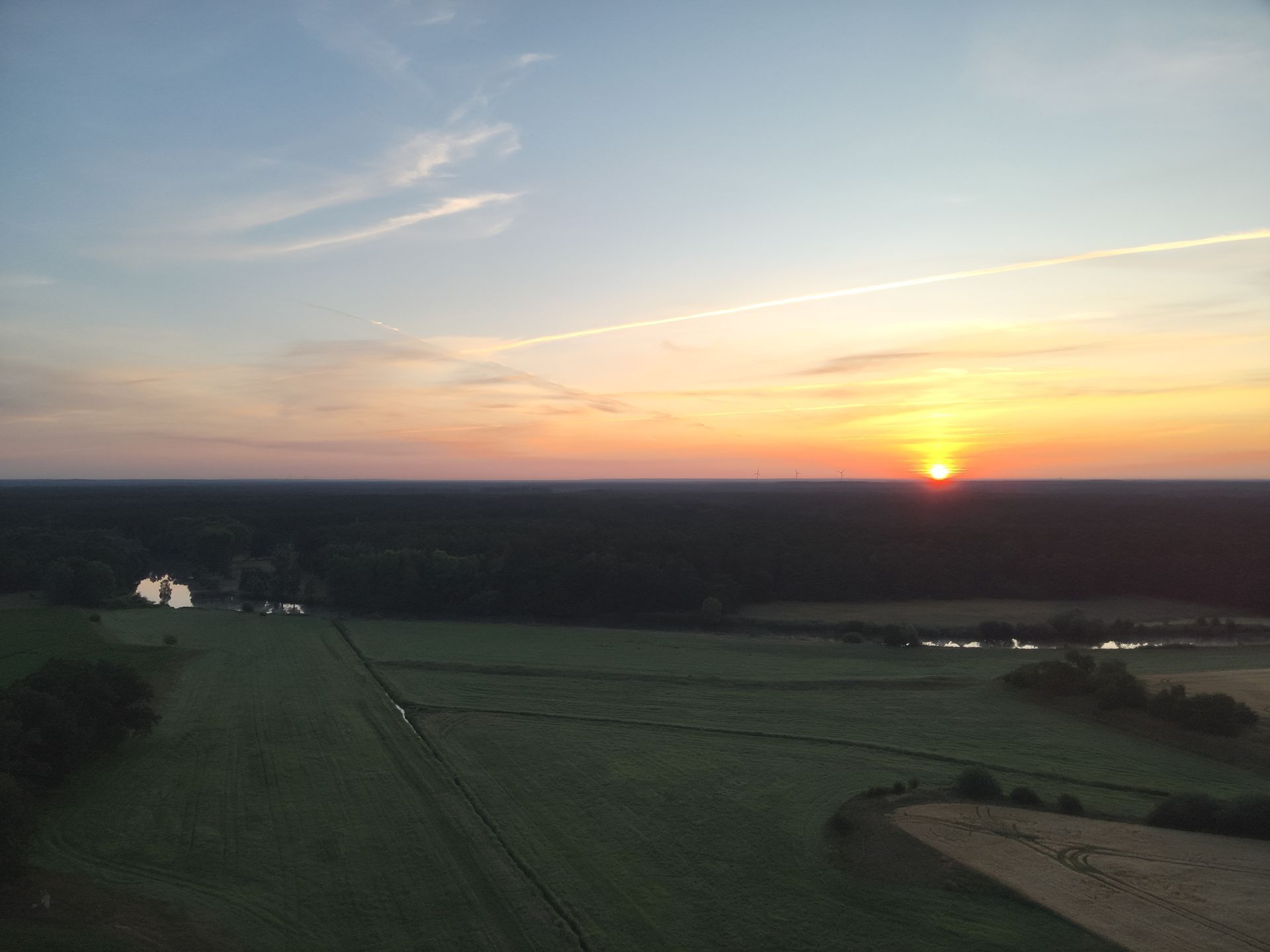 Sonnenuntergang über Feldern und Wäldern. Der Himmel ist blau und orange.