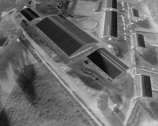 Luftaufnahme eines Bauernhofs mit langen Gebäuden und Solarmodulen.