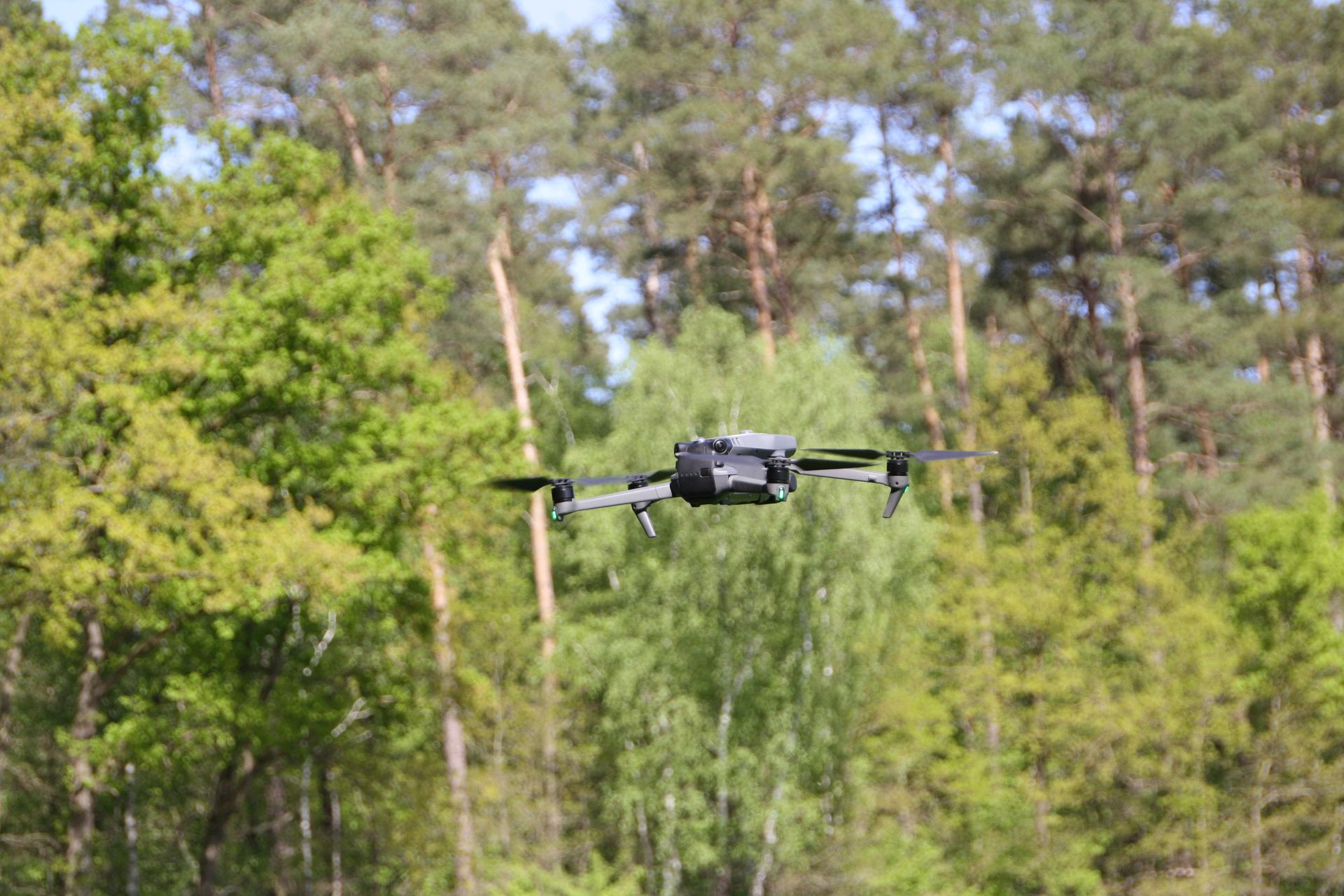 Drohne fliegt mitten in der Luft vor einem grünen Baumhintergrund und blauem Himmel.