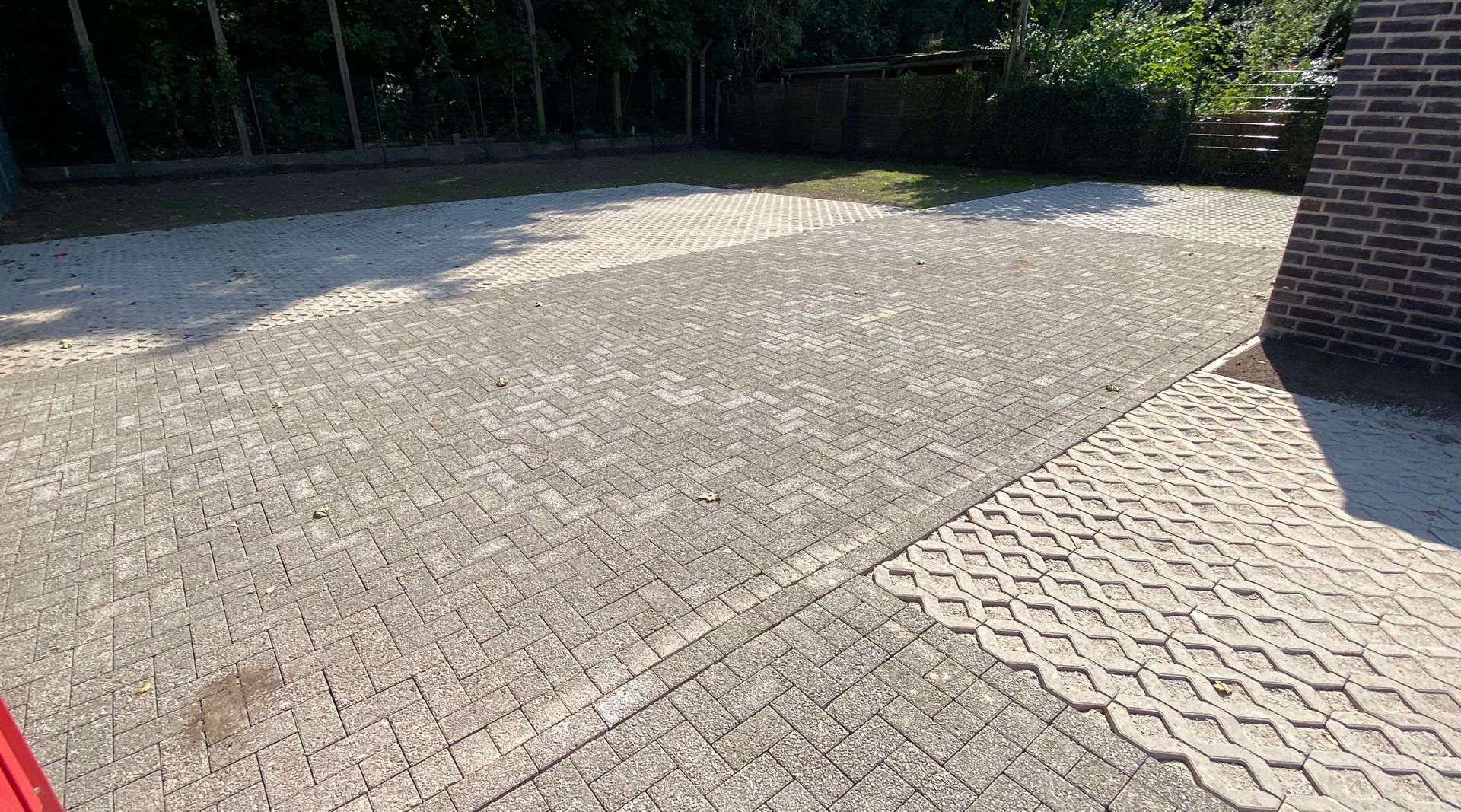 Ein rotes Auto steht in einer Einfahrt neben einem Backsteingebäude.