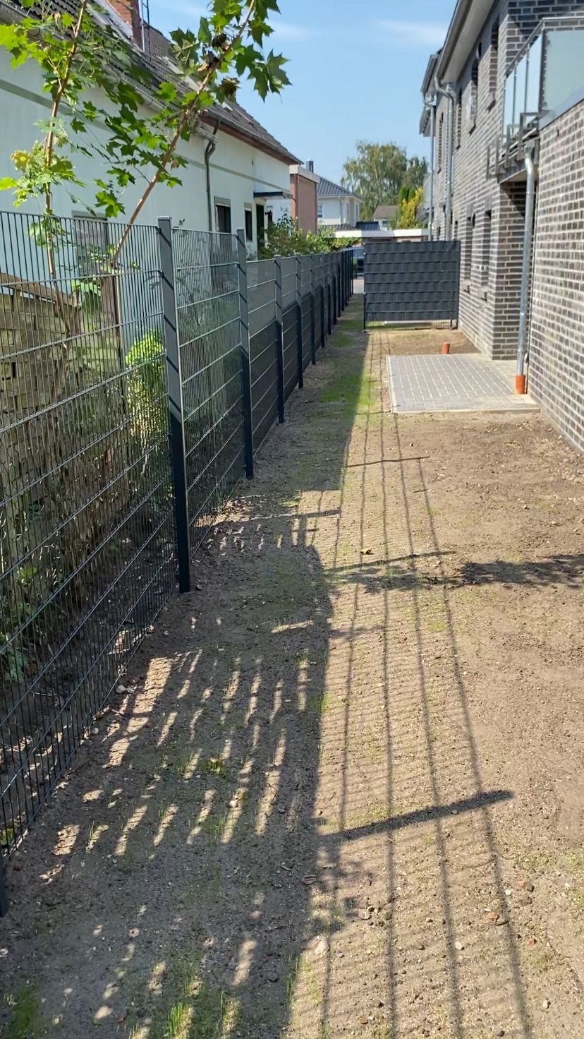 Ein Zaun entlang eines Gehwegs, der zu einem Haus führt.