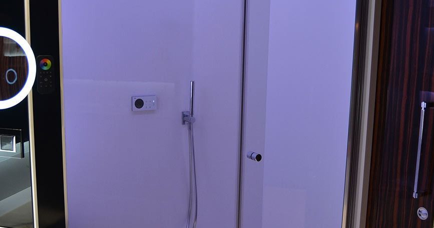 Pared blanca del pasillo con un pequeño dispositivo montado, cables y una puerta que da a una habitación con poca luz.