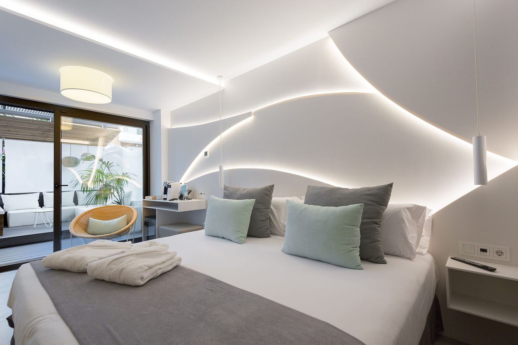 Dormitorio moderno blanco con una cama grande, iluminación tenue y una puerta corrediza de cristal que da a un balcón.