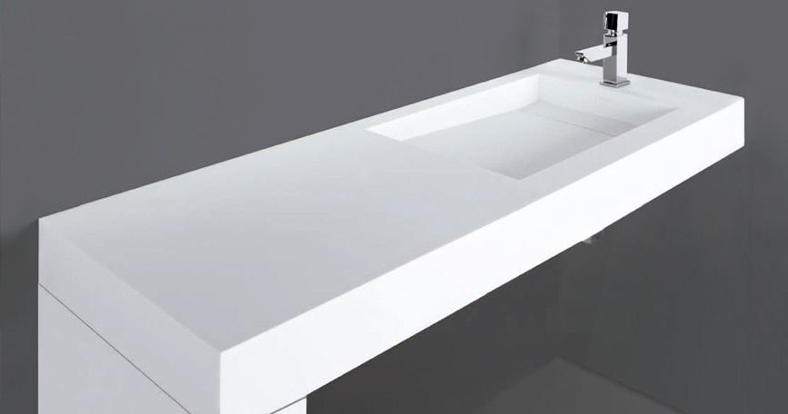 Encimera de lavabo de baño moderna blanca con lavamanos integrado y grifo cromado sobre fondo gris.