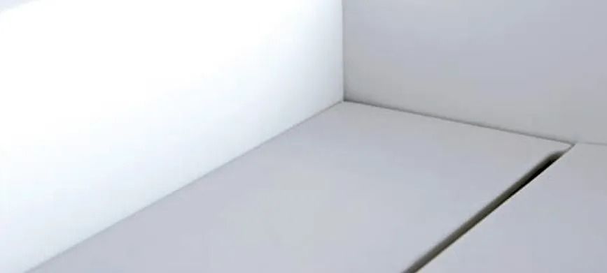 Rincón de habitación minimalista blanco con una superficie blanca lisa y una junta o hueco oscuro.
