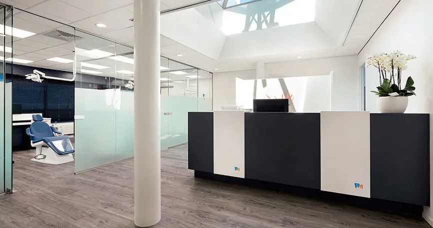 Vestíbulo de oficina moderno con paredes de cristal, techo blanco, mostrador de recepción oscuro y sillones azules.